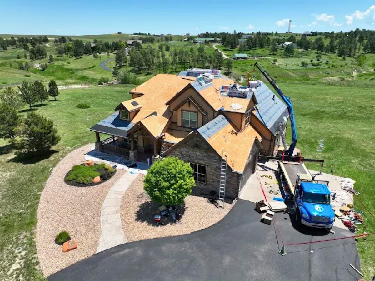 Estate home roof replacement with crane delivering materials on scenic hillside