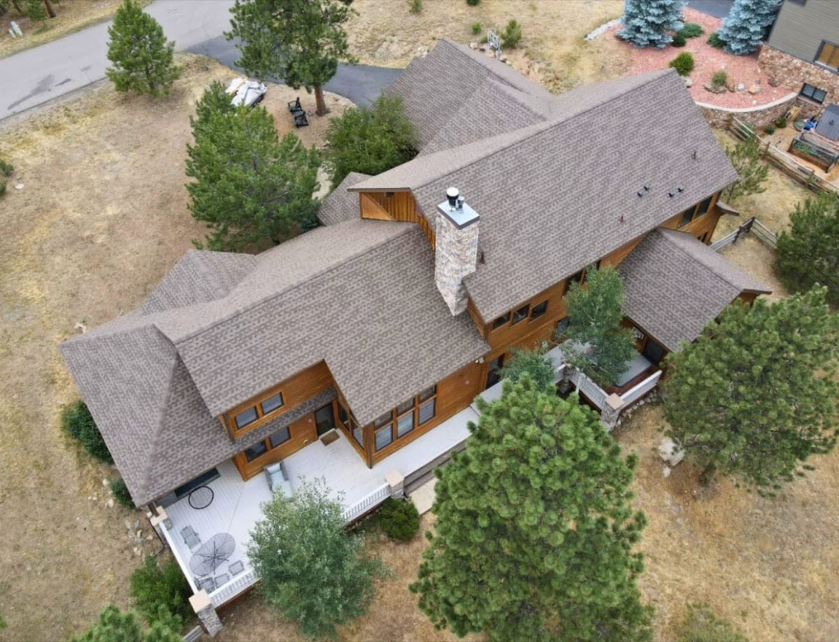 Mountain home with completed shingle roof nestled among pine trees