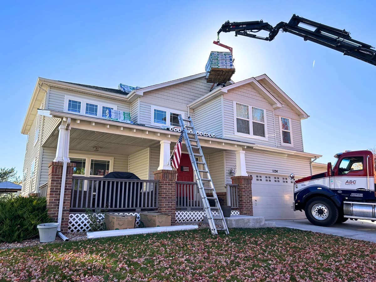 Crane delivering shingle bundles to residential roof replacement project