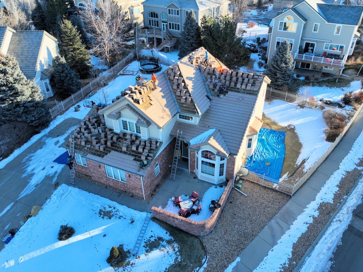 Tile roof installation in progress during winter with stacked materials