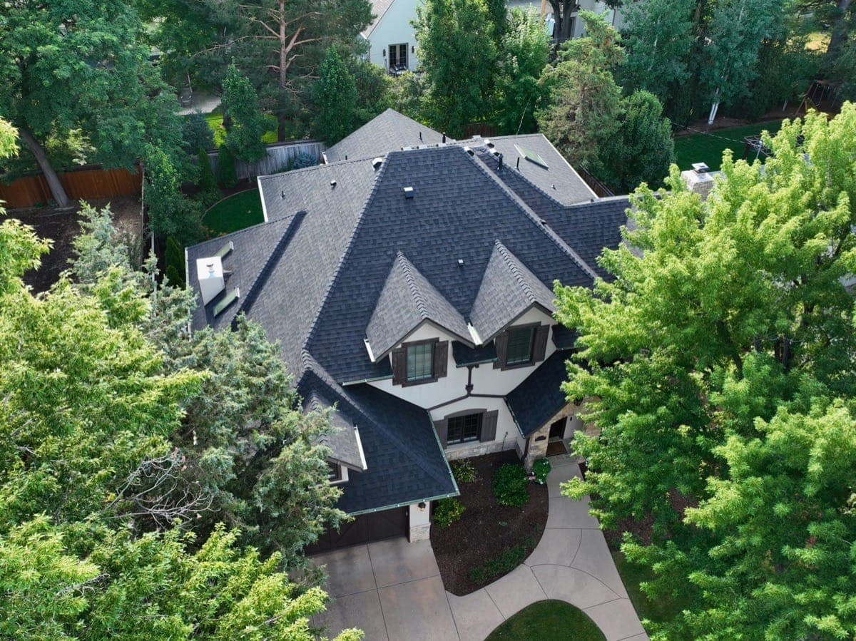 Completed luxury home with dark designer shingle roof surrounded by trees